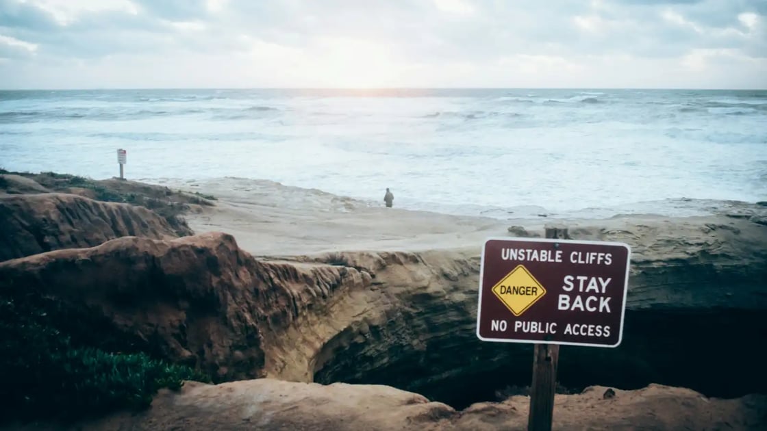 Photo of Stay back sign over cliffs and as man looks over a stormy sea by Robert Gourley on Unsplash